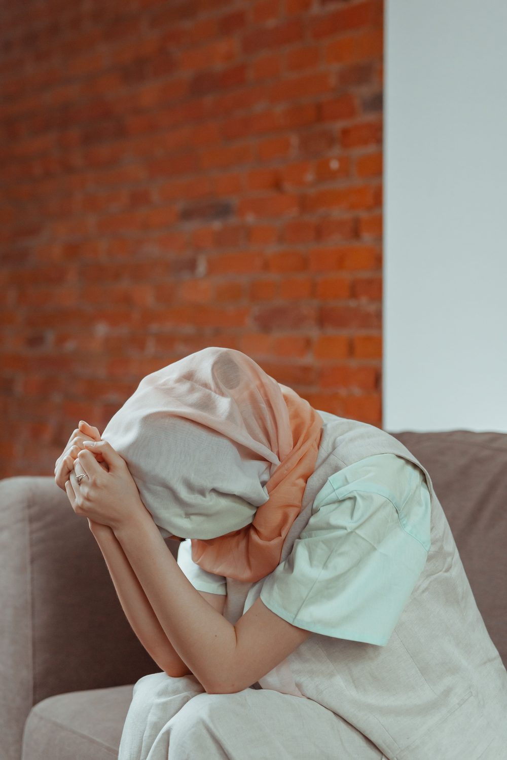 A person on a sofa hiding under a scarf